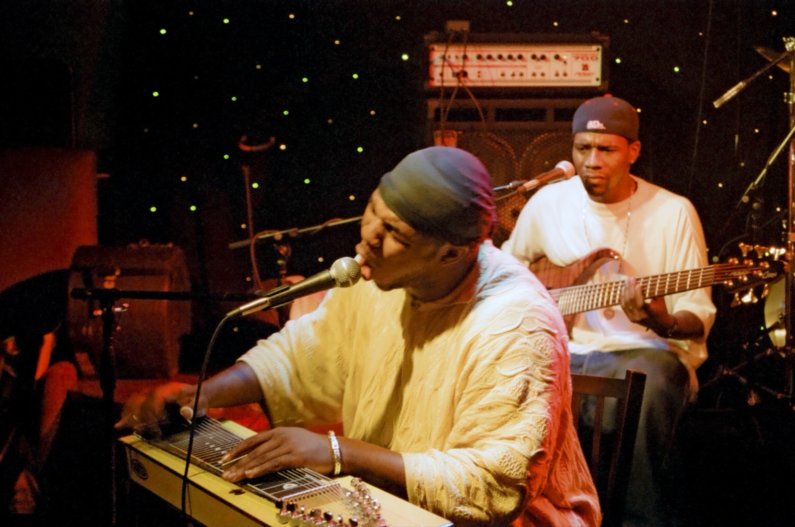 Robert Randolph sings into a microphone over his pedal steel while the bassist plays behind him against a starry backdrop.